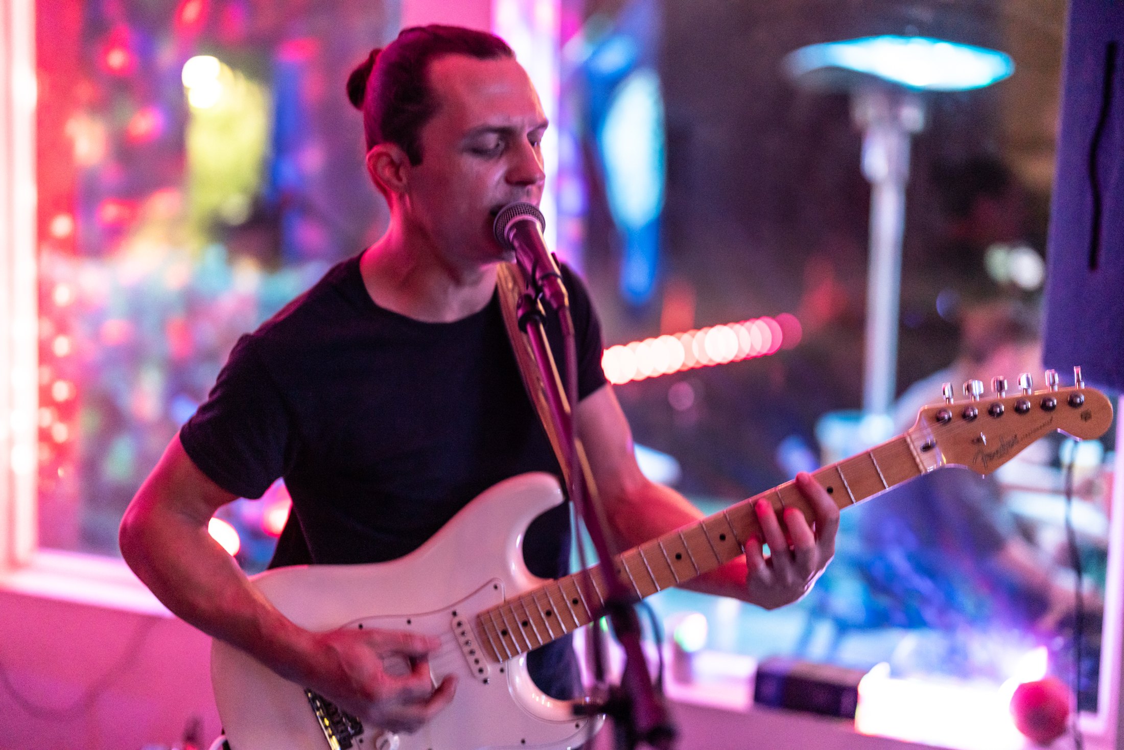 Eric Stockton singing and playing guitar under pink stage lights